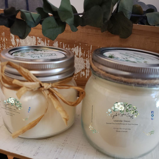 2 soy candles in glass jars, size 8oz and 10oz.  Each jar has raffia bows tied around their necks. Background shows eucalyptus leaves. The scent sold in these jars is Lavender Dream.